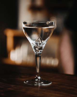 Antique wine glass holds a clear cocktail, a simple visual drink that is a joy to sip