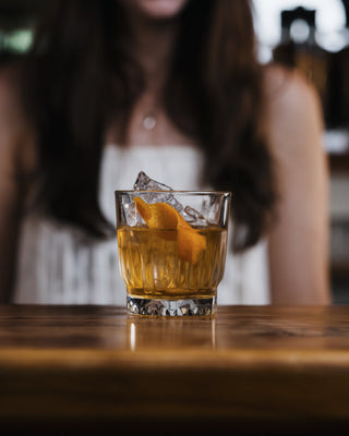Short glass holds large square ice cubes and a decadant vibrant orange cocktail of Greenstone Gin and Tangelo Liqueur