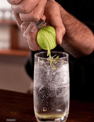 A tall glass filled with Lime Gin FIzz is garnished with strips of lime zest