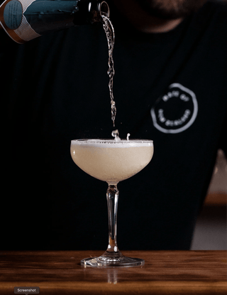 Champange is poured from a height into a martini glass splashing as it fills, a bubbly visually striking cocktail