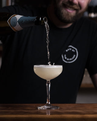 Champange is poured from a height into a martini glass splashing as it fills, a bubbly visually striking cocktail