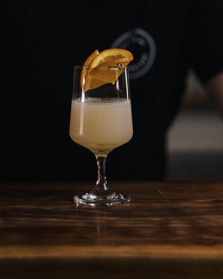 Hands place the final touch of a orange round on top of this beautful cocktail made with CHmapionz Gin and Apricot Liqueur