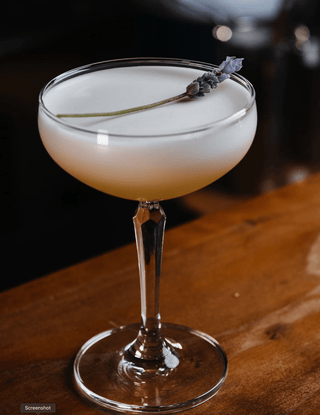 A lavender sprig rests lightly on the Bee's Knees, a stunning cocktail presented in a martini glass on a wooden bar