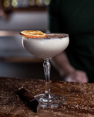 Thick creamy cocktail in a martini glass, garnished with dried orange round and grated chocolate