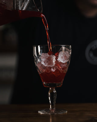 Pouring ruby red cocktail into glass on bar top
