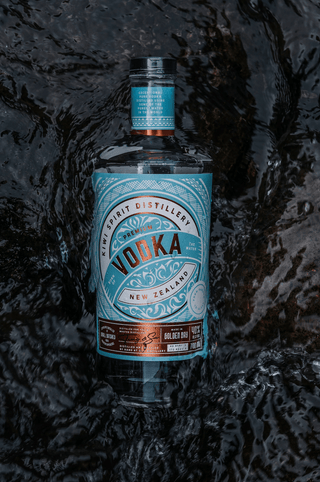 Premium New Zealand Vodka in clean running water, water washing over the label