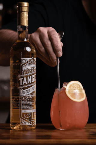 Jeremy stiring a Ruby Tuesday cocktail with a bottle of Tangelo Liqueur