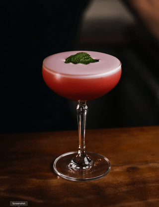 Red foamy cocktail with a mint leaf garnish, boysenberry sour presented in a martini glass