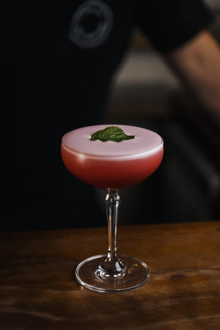 Red foamy cocktail with a mint leaf garnish, boysenberry sour presented in a martini glass