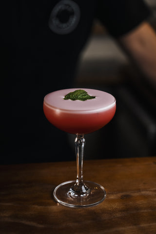 Red foamy cocktail with a mint leaf garnish, boysenberry sour presented in a martini glass