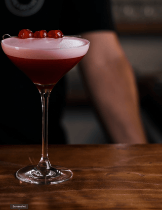 Clover Club presented in a martini glass with line of candied fruit as a garnish, a ruby red cocktail with froth