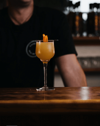 Delightfully Ginger cocktail presented on a wooden bar in a wine glass with a orange twist garnish