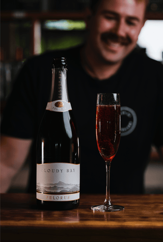 A champange glass of bright red Kir Royal presented alongside a bottle of Cloudy Bay Brut, a stunning boysenberry cocktail