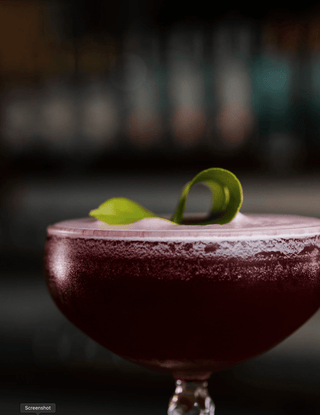 Close up shot of a martini glass with a deep purple Motupipi Martini cocktail, a delicate lime leaf garnishes 