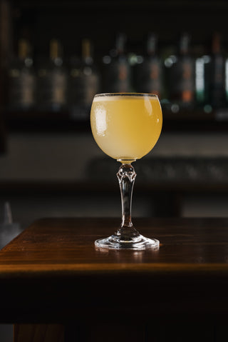 Perfect lighting highlights the beauty of this stunning cocktail, a rounded wine glass holding the yellow cocktail is garnsihed with fragrent fresh orange oil