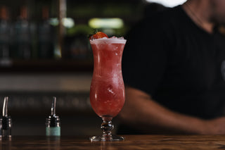 A pink cocktail garnished with fresh starwberries, in a tall glass on a wooden bar