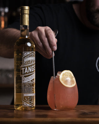 Jeremy stirs a short round glass holding the Ruby Tuesday cocktail, a bottle of Tangelo Liqueur is presented alongside