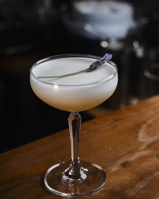 A lavender sprig rests lightly on the Bee's Knees, a stunning cocktail presented in a martini glass on a wooden bar