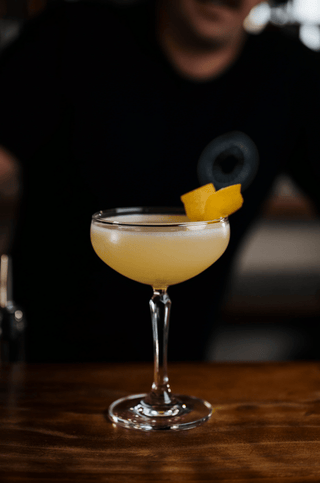 Martini glass on a bar holding a beautiful Breakfast Martini, orange peel garnish