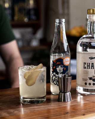 A short glass filled with the GG is pictured alongside a metal cocktail measurer, Karma Cola Ginger Beer and Championz Gin