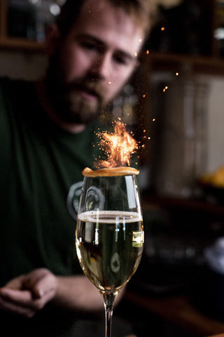 Fire burns on a dried orange slice balanced on top of a champange glass filled with The Italian Job