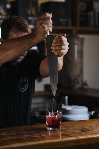 Lemon being squeezed on a large knife into a short cocktail glass with Boysenberry Buck