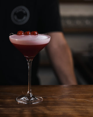 Clover Club presented in a martini glass with line of candied fruit as a garnish, a ruby red cocktail with froth