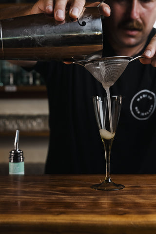 Jeremy pours the Katinka cocktail into glass on wooden bar