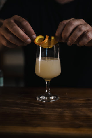 Hands place the final touch of a orange round on top of this beautful cocktail made with CHmapionz Gin and Apricot Liqueur