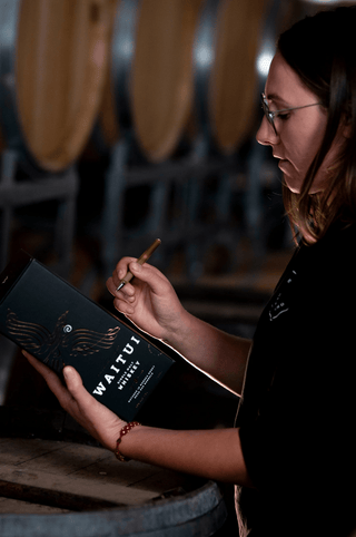 Person hand writing the batch number and bottle number on a box of Waitui Whiskey